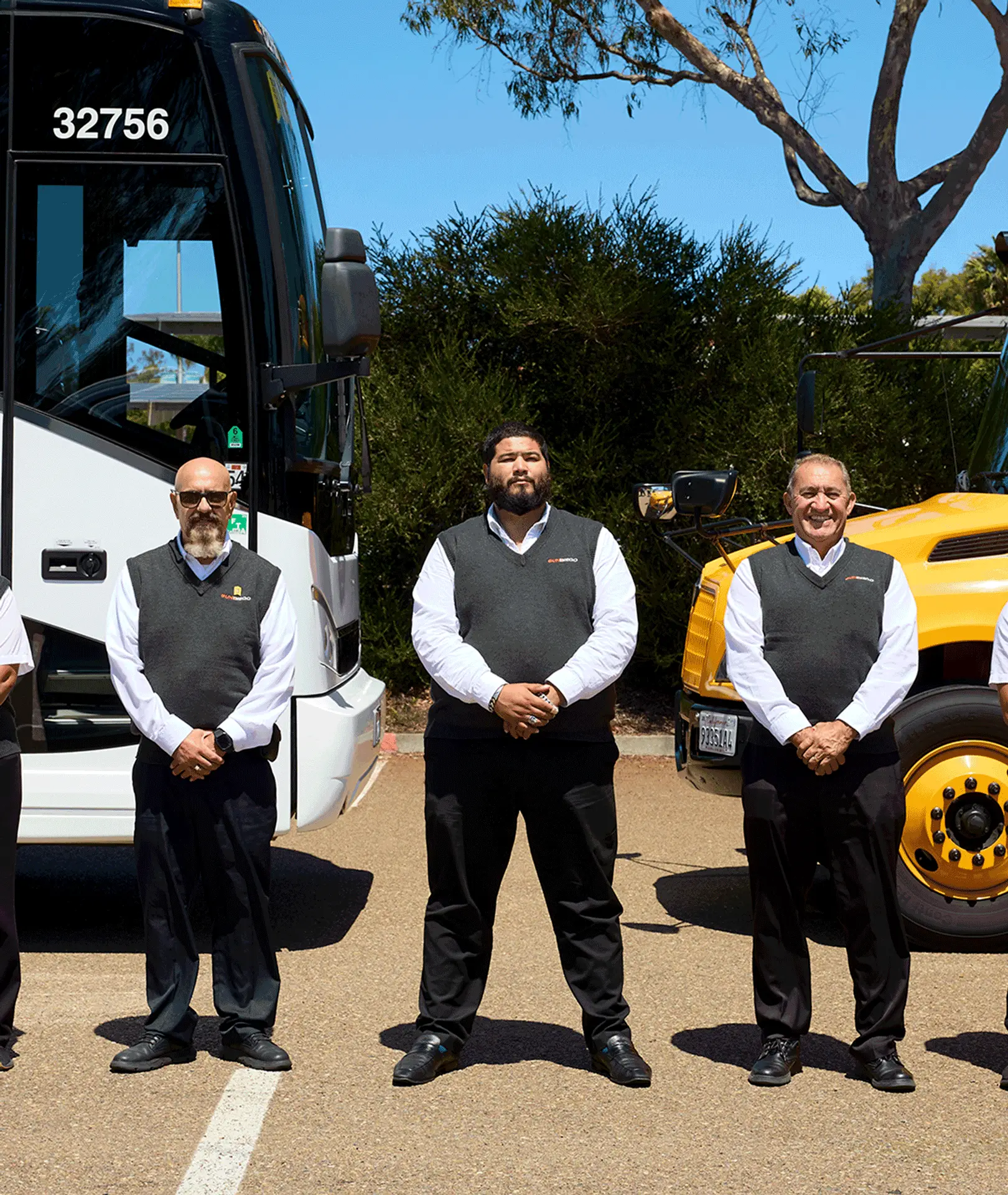 Three uniformed Sun Diego Charter team members standing beside a motorcoach and school bus