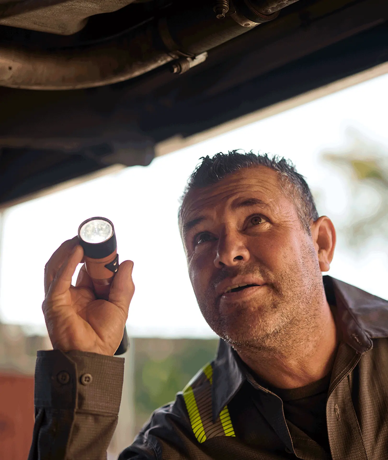 Maintenance technician inspecting the underside of a vehicle with a flashlight