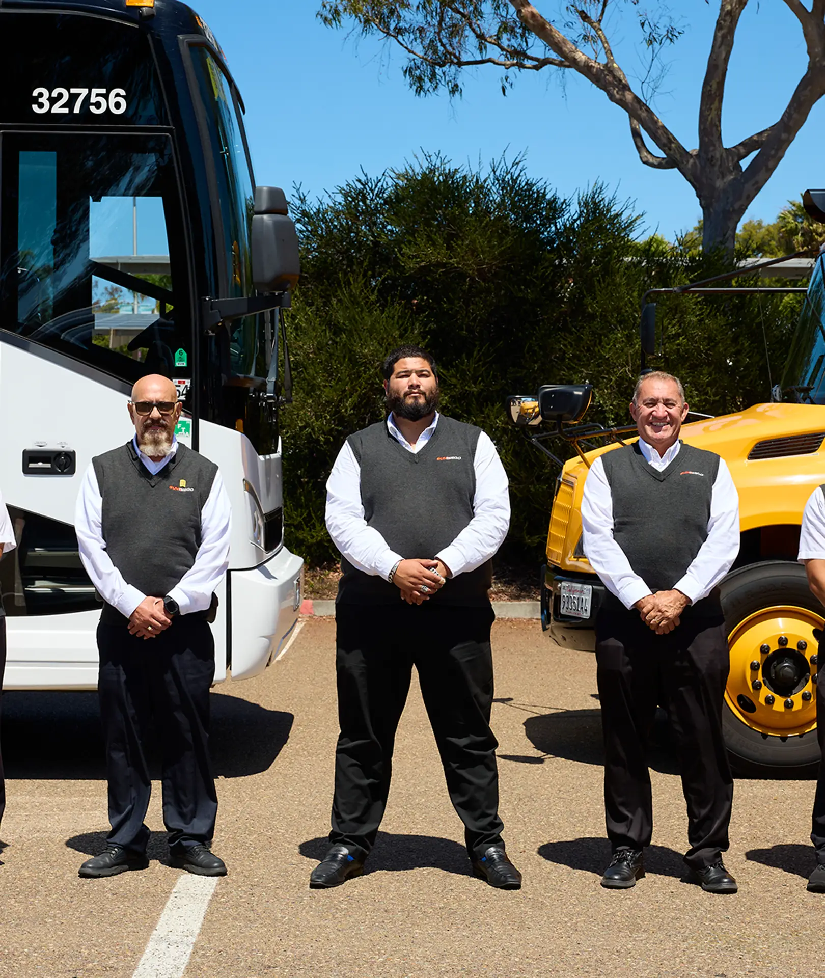 Three uniformed Sun Diego Charter team members standing beside a motorcoach and school bus