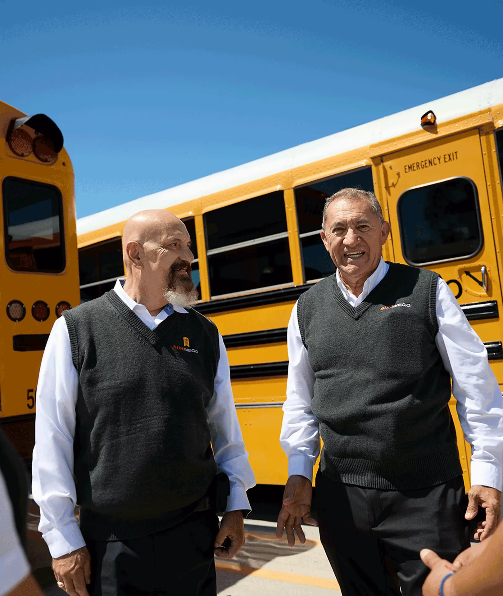 Two uniformed team members standing beside a yellow school bus