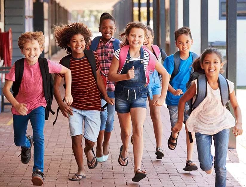 Children carrying backpacks walking together outside a school