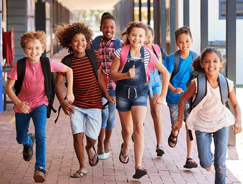 Children carrying backpacks walking together outside a school